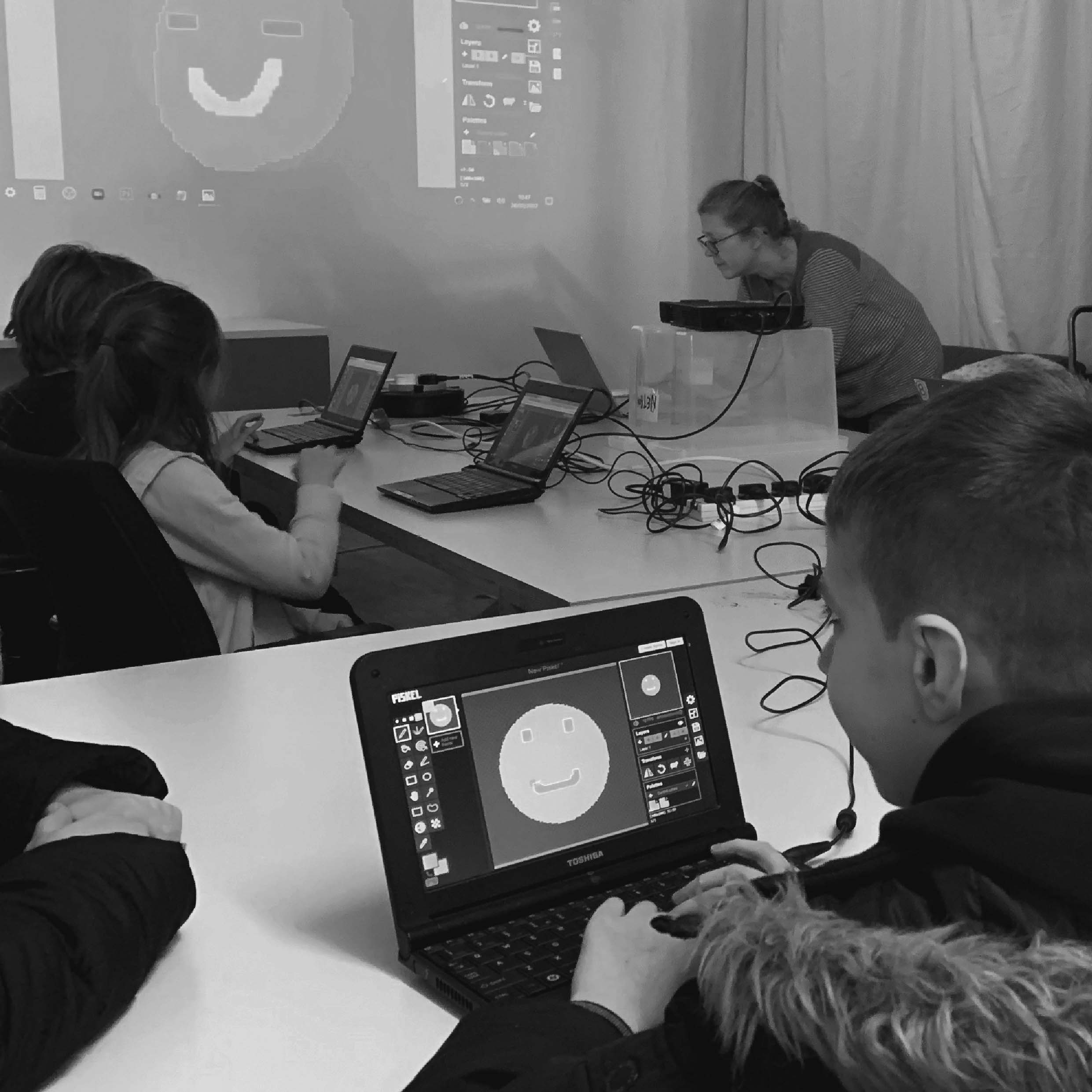 Children sitting with laptops drawing smiley faces with code